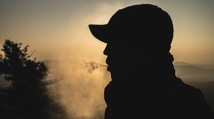 silhouette of a guy producing a cloud of smoke from a vaporizer
