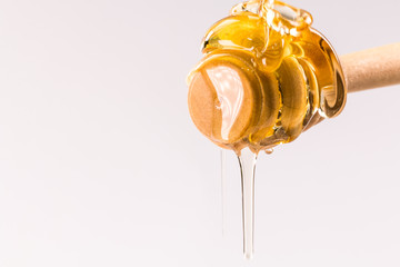 Honey dripping from a wooden honey dipper isolated on white