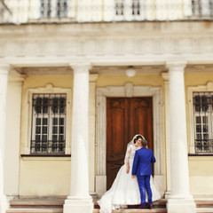 Groom in blue suit kisses bride while she stands before old wood