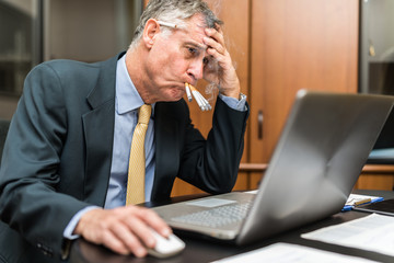 Nervous businessman smoking a lot of cigarettes at once while looking at his computer