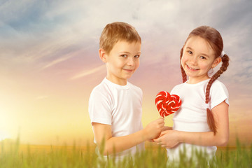 Kids, boy gives a little girl candy red lollipop in heart shape outdoor