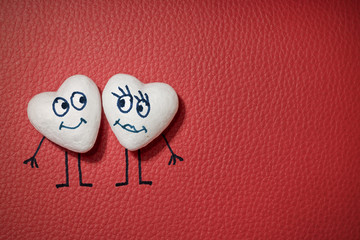 Two white hearts with happy faces on red leather background
