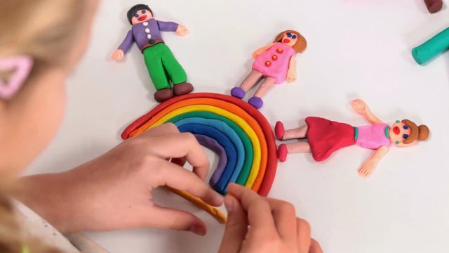Happy people over the rainbow made from modeling clay - little girl completing an art project