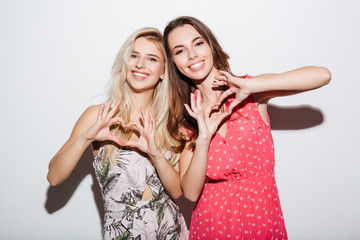 Two smiling girls in dresses showing heart gesture with hands