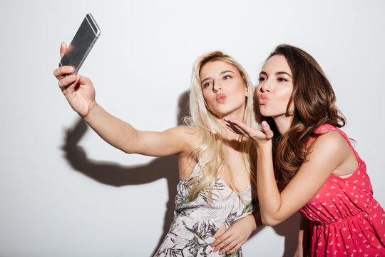 Friends taking selfie with smartphone and blowing kiss to camera