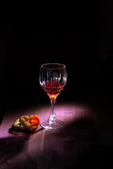 crystal glass with red wine is on the table of A red or sauna on a dark background are a number of chocolates in the shape of hearts sprinkled with almond nuts. romantic photo