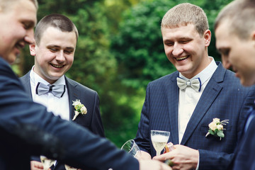 Charming boys dressed for wedding laughs while they drink champagne