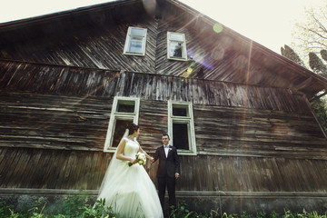 Bright morning sun shines over wooden house before which wedding couple stands
