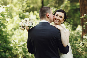 Groom kisses bride's cheek tender while they kiss in the forest