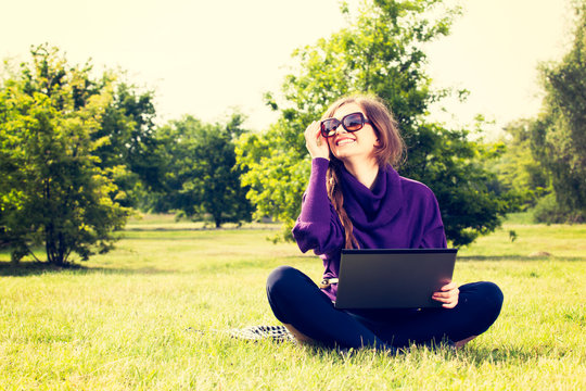 Young woman using laptop in the park sitting on the green grass