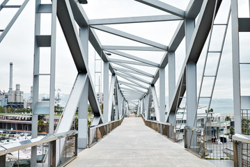 Walking industrial bridge with huge steel supports and geometrical shape above the yacht port is leading to processinc factory, landscape view