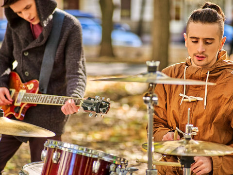 Festival music band. Cropped shot of male musicians playing on percussion instruments in city park . Drums with sticks and guitar closeup.