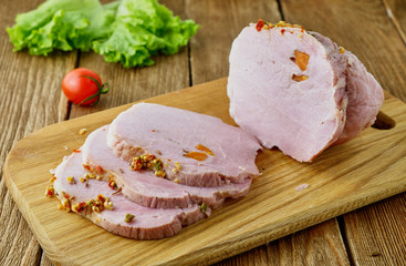 Sliced cold baked pork with vegetables on a wooden background
