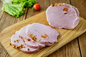 Sliced cold baked pork with vegetables on a wooden background