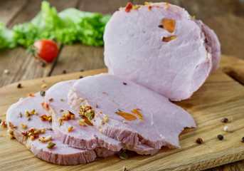 Sliced cold baked pork with vegetables on a wooden background