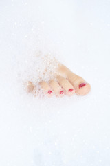Closeup of childs feet washing in bathroom with shampoo foam on it. Nails painted red
