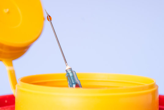 Yellow medical disposal waste box, syringe needle with red drop on the tip