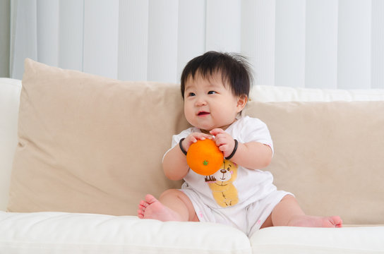 Asian baby holding an orange