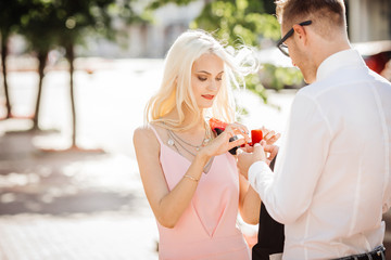 young man giving diamond engagement ring in little red box to woman