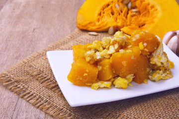 stir-fried pumpkin with eggs and fresh cut pumpkin on wooden background.