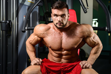 Brutal strong bodybuilder man pumping up muscles and train gym