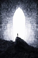 Surreal dark cave landscape. Man silhouette on cliff and cave entrance in the background