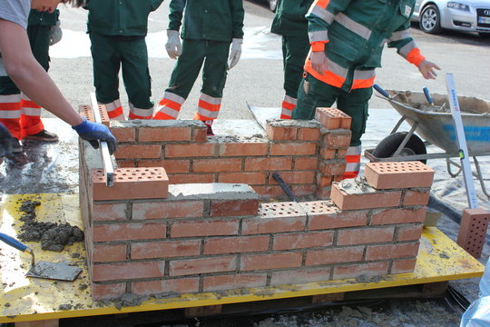 Lehrlinge: Auf einer Baustelle wird eine Mauer aus Ziegelsteinen aufgestellt
