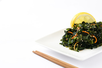 Wakame salad with carrot, sesame seeds and lemon juice in plate isolated
