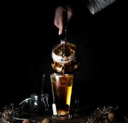 female hand pours tea from a golden kettle. black background