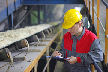 Worker controlling and writing the result of the quality of chopped sugar beet on conveyor belt in sugar refinery