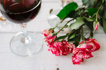 Red Valentine's day roses and glass of wine on white table