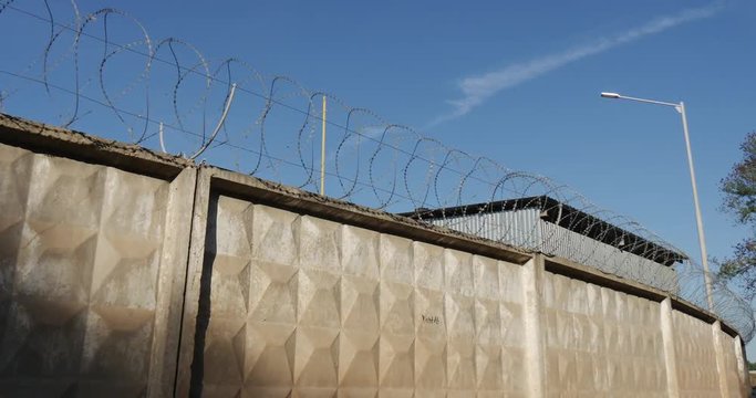 High Concrete Fencel With Rolls of Bard Wire at Oil Storage Facilities With a White Car of Inspectors Before It, Being Shot From a Moving Car