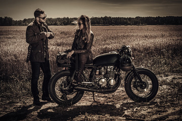 Obraz na płótnie Canvas Young, stylish cafe racer couple on vintage custom motorcycles in field