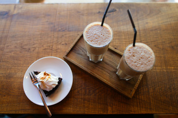 Two coffee drinks with drinking straw and slice of pie on saucer