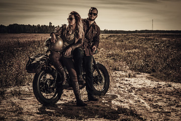 Obraz na płótnie Canvas Young, stylish cafe racer couple on vintage custom motorcycles in field