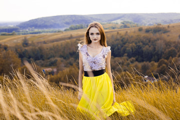 Beautiful fashionable pretty gorgeous girl in dress on the flowers field. Nice girl with wreath of flowers on her head and bouquet of many yellow flowers sitting on meadow yellow field in summertime.