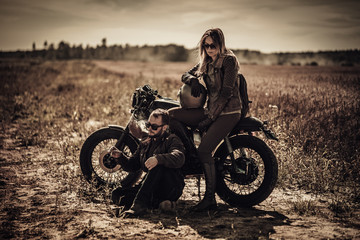 Fototapeta na wymiar Young, stylish cafe racer couple on vintage custom motorcycles in field