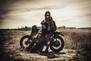Young, stylish cafe racer couple on vintage custom motorcycles in field