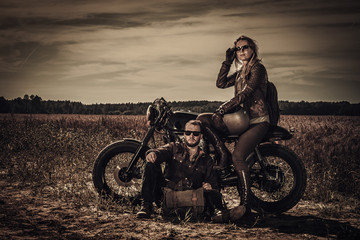 Fototapeta na wymiar Young, stylish cafe racer couple on vintage custom motorcycles in field
