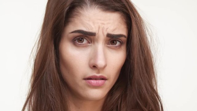 Skeptical beautiful Caucasian female standing on white background looking forward with disappointment in slowmotion. Close up footage