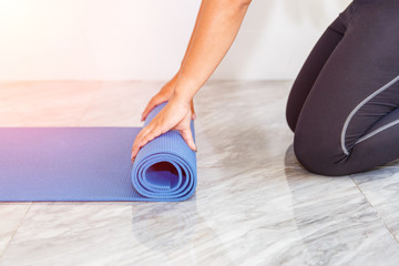Close-up of attractive young woman folding blue yoga or fitness mat after working out at home in...