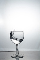 Transparent glass cup with a pouring bubbling cold fresh water with bubbles and drops