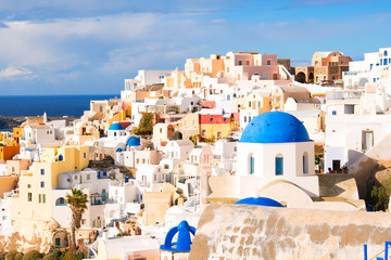 View of the seaside on a summer day. .Numerous white cottages cover the high seashore on the background of blue water..Panorama of Oia village with colorful houses   - obrazy, fototapety, plakaty