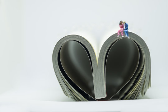 Miniature people, young couple sitting on the book in heart shape