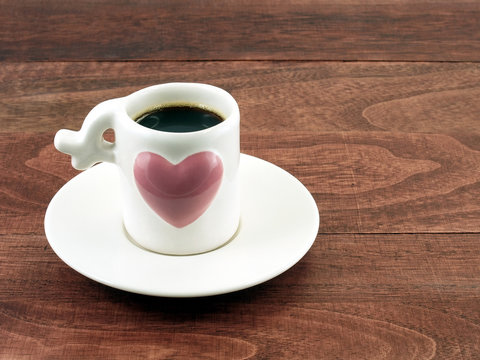 espresso shot in coffee cup with embossed big purple heart and saucer on brown rustic desk floor with copy space