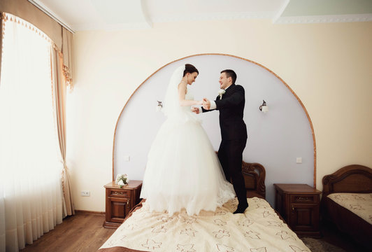 young and happy bride and groom jumping on the bed