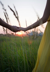 Young couple in love meets a summer sunset in field holding hands among the ears of corn. Love. A family. Forever.