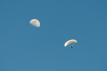 Paragliding with the moon in the blue sky at daylight
