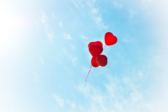 Inflatable helium balloons in the form of red hearts on a blue summer sky. Bunch of balloons rising into the sky. Love.