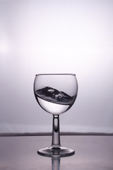 Transparent glass cup with a pouring bubbling cold fresh water with bubbles and drops